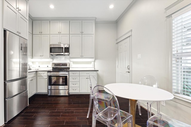 kitchen featuring dark wood-type flooring, crown molding, tasteful backsplash, stainless steel appliances, and white cabinets