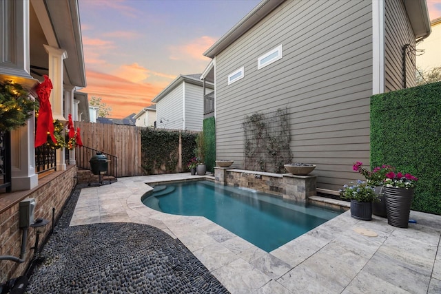 pool at dusk featuring pool water feature and a patio