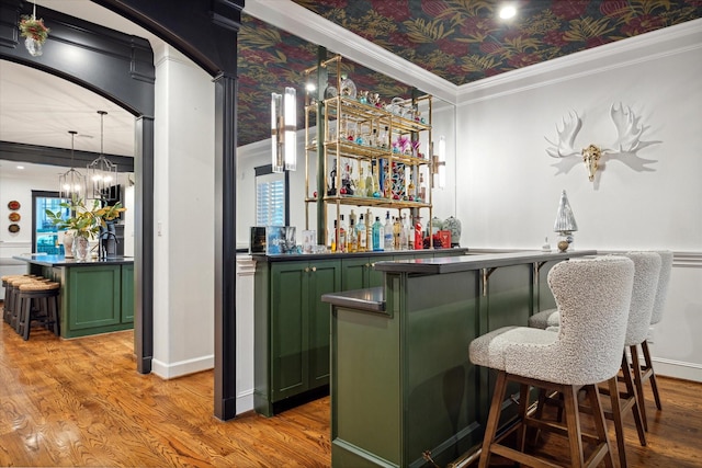 bar with pendant lighting, crown molding, light hardwood / wood-style floors, and green cabinets