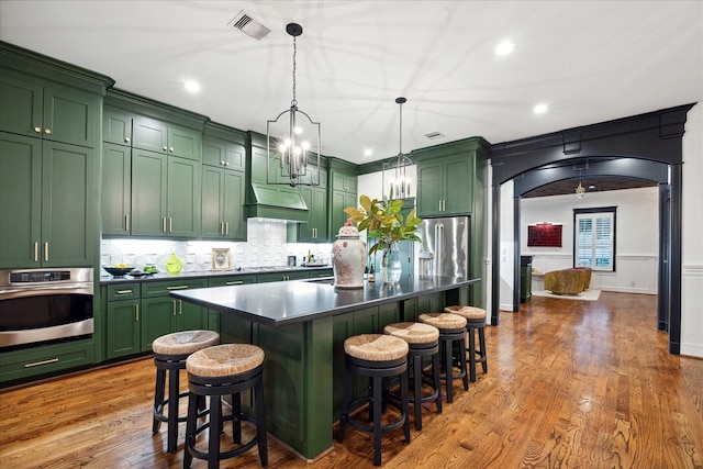 kitchen featuring a center island with sink, pendant lighting, green cabinets, and stainless steel appliances