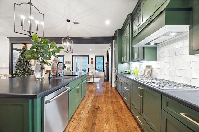 kitchen featuring stainless steel appliances, an island with sink, wall chimney exhaust hood, and green cabinets