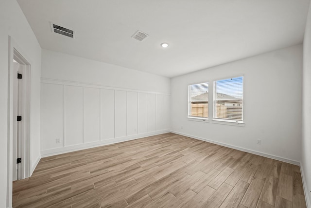 spare room featuring light wood-style flooring, visible vents, and a decorative wall