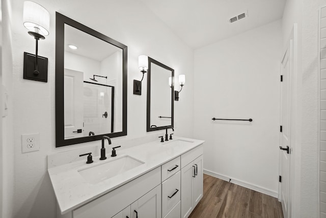 full bath featuring a stall shower, double vanity, a sink, and wood finished floors