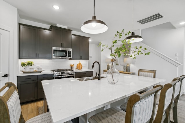 kitchen with light wood finished floors, visible vents, decorative backsplash, appliances with stainless steel finishes, and a sink