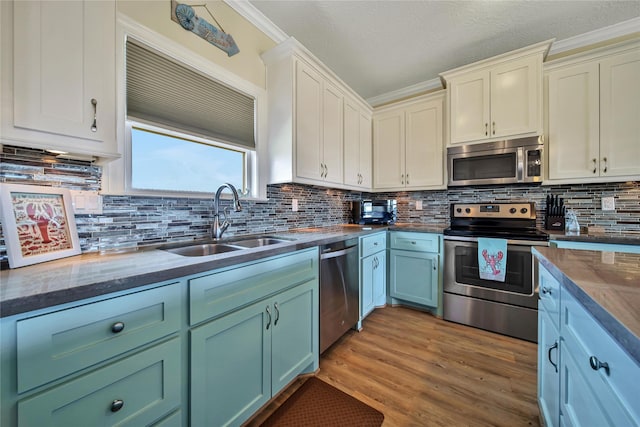 kitchen with appliances with stainless steel finishes, tasteful backsplash, sink, crown molding, and light wood-type flooring