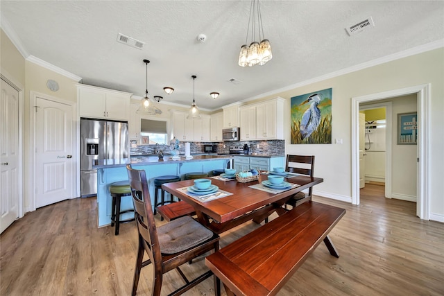 dining area featuring crown molding, light hardwood / wood-style floors, a chandelier, and a textured ceiling