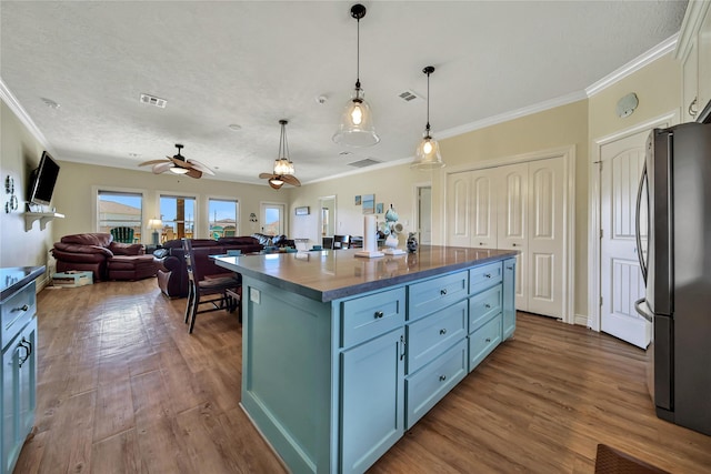 kitchen featuring stainless steel refrigerator, wood-type flooring, hanging light fixtures, ornamental molding, and a center island