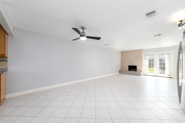 unfurnished living room with light tile patterned floors, a large fireplace, ceiling fan, and french doors