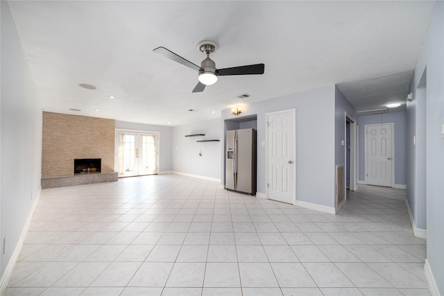 unfurnished living room featuring light tile patterned flooring, a large fireplace, and ceiling fan