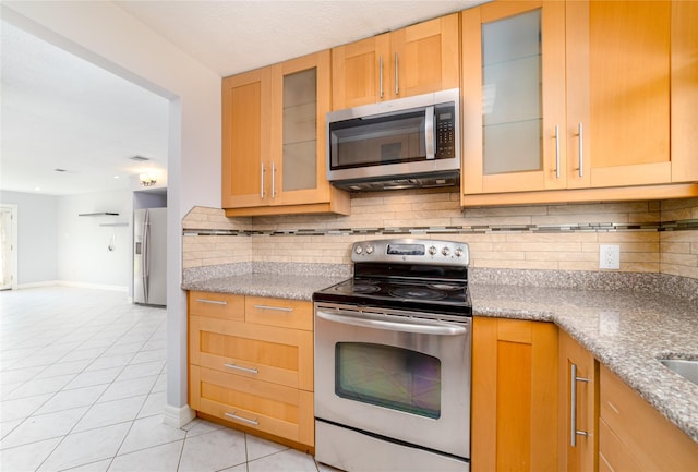 kitchen with light stone countertops, appliances with stainless steel finishes, light tile patterned floors, and backsplash