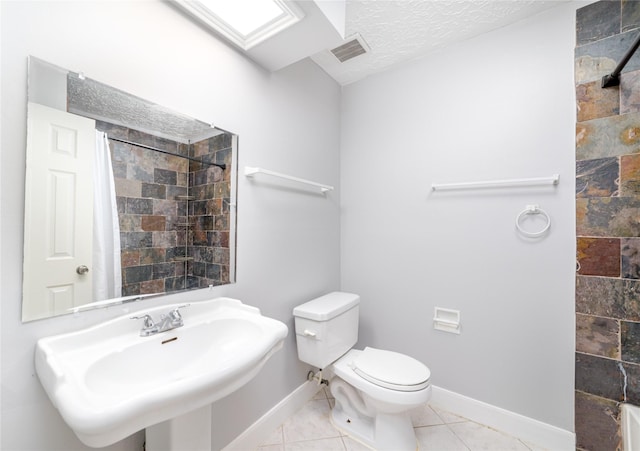 bathroom with a skylight, sink, toilet, tile patterned floors, and a textured ceiling