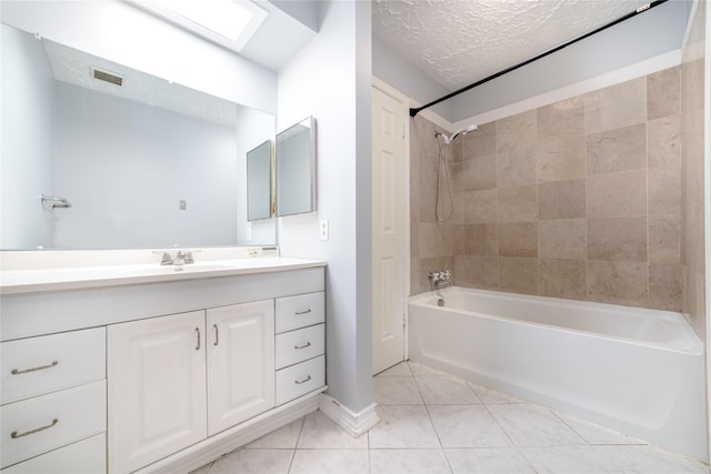 bathroom with tile patterned floors, a skylight, a textured ceiling, vanity, and tiled shower / bath combo