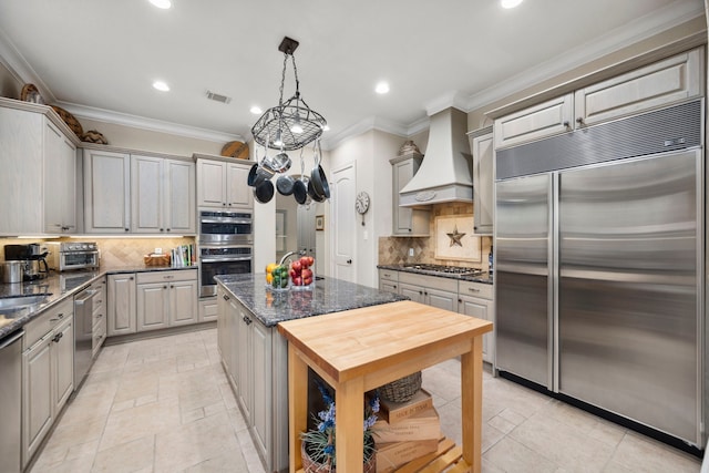 kitchen featuring gray cabinets, premium range hood, appliances with stainless steel finishes, decorative light fixtures, and dark stone countertops