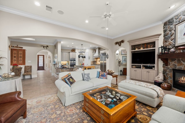 living room featuring crown molding, a stone fireplace, and ceiling fan