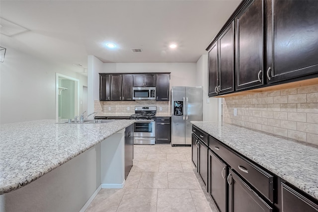 kitchen with dark brown cabinetry, sink, tasteful backsplash, stainless steel appliances, and light stone countertops