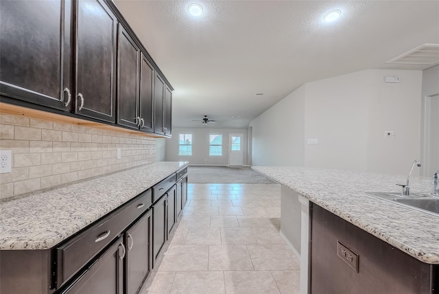 kitchen with sink, backsplash, light tile patterned floors, ceiling fan, and a center island with sink