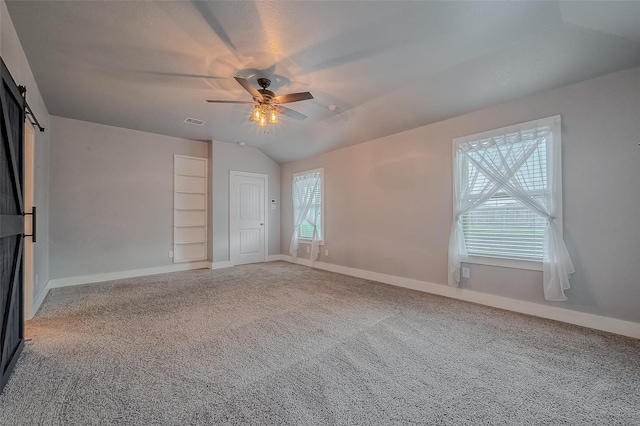 carpeted empty room with vaulted ceiling, a barn door, and ceiling fan