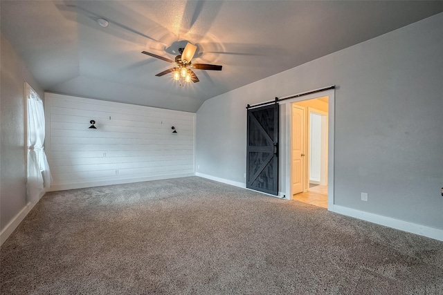 spare room featuring light carpet, lofted ceiling, a barn door, and ceiling fan