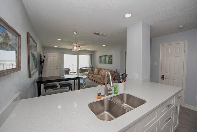 kitchen featuring dark wood-type flooring, sink, white cabinetry, light stone counters, and a textured ceiling