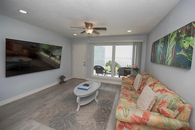 living room featuring wood-type flooring, ceiling fan, and a textured ceiling