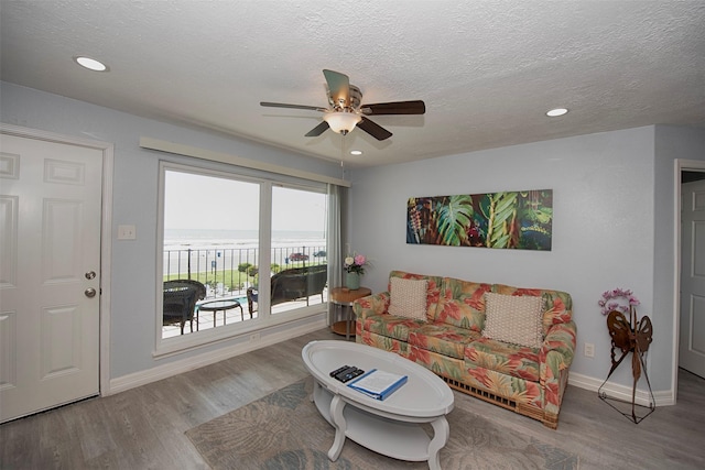 living room with ceiling fan, hardwood / wood-style flooring, a textured ceiling, and a water view