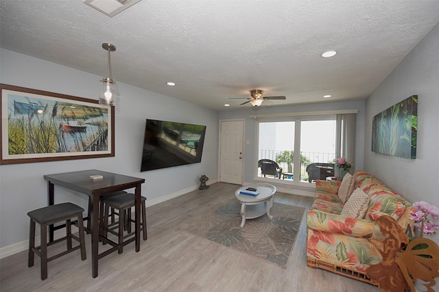 living room featuring ceiling fan, light hardwood / wood-style floors, and a textured ceiling