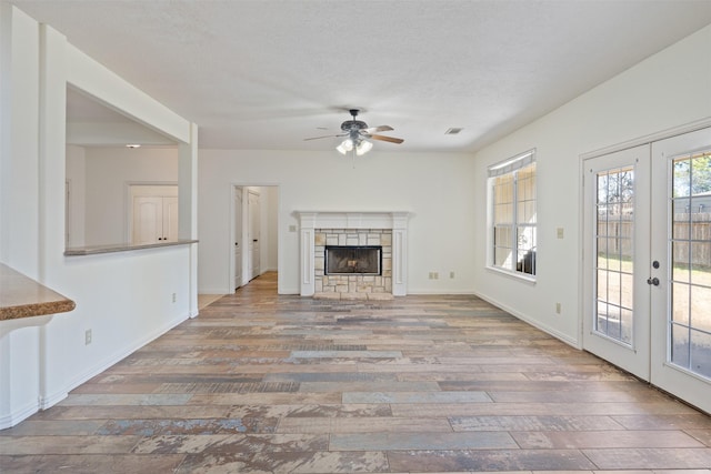 unfurnished living room featuring french doors, a stone fireplace, a textured ceiling, hardwood / wood-style flooring, and ceiling fan