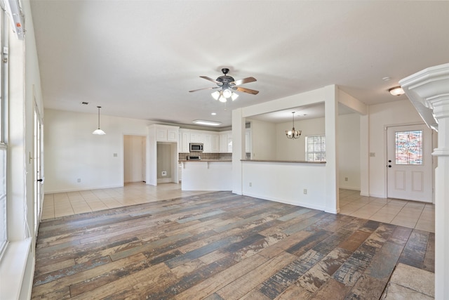 unfurnished living room with ceiling fan with notable chandelier and light hardwood / wood-style flooring