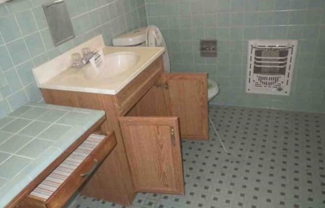 bathroom featuring vanity, heating unit, tile walls, and toilet