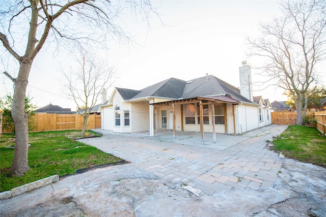 rear view of property featuring a chimney, a patio area, a yard, and a fenced backyard