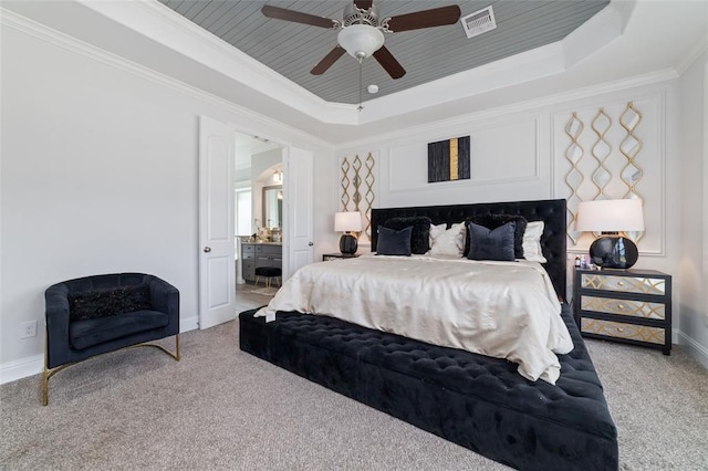 carpeted bedroom with ornamental molding, connected bathroom, ceiling fan, and a tray ceiling