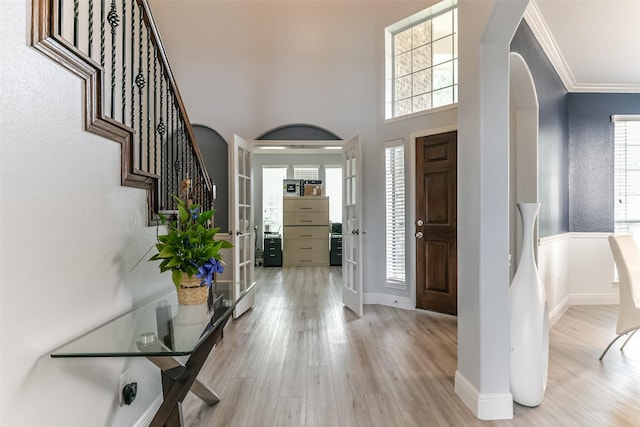 foyer entrance featuring light hardwood / wood-style flooring, ornamental molding, a high ceiling, and plenty of natural light