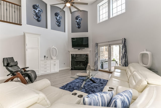 living room with a high ceiling, ceiling fan, a high end fireplace, and light hardwood / wood-style floors