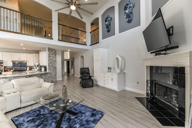 living room with light hardwood / wood-style flooring, a fireplace, ceiling fan, and a high ceiling