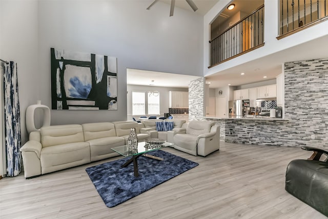 living room with ceiling fan, a high ceiling, and light wood-type flooring