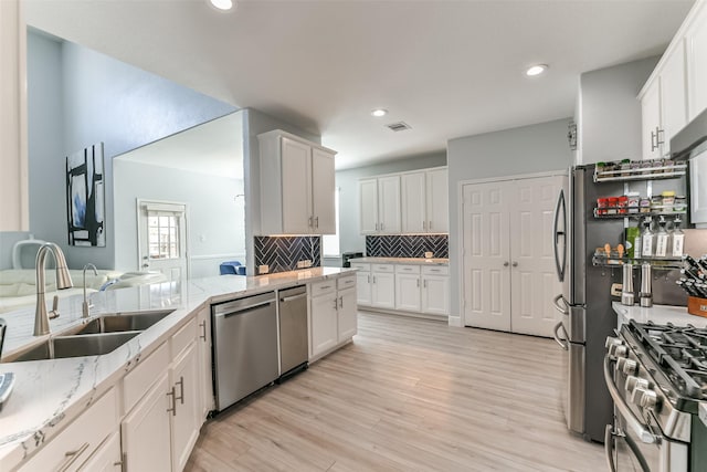 kitchen featuring appliances with stainless steel finishes, white cabinetry, sink, backsplash, and light stone counters