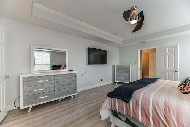 bedroom featuring crown molding, a tray ceiling, ceiling fan, and light wood-type flooring