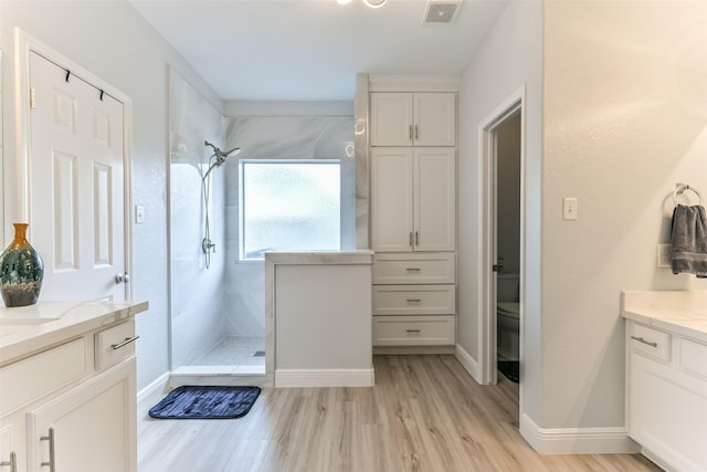 bathroom with a tile shower, vanity, hardwood / wood-style flooring, and toilet