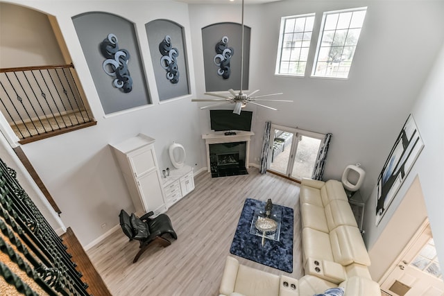 living room featuring ceiling fan, a high end fireplace, light hardwood / wood-style floors, and a towering ceiling