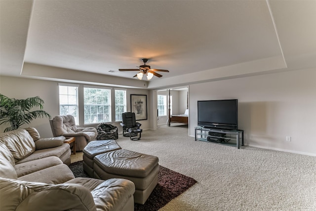 living room with a tray ceiling, carpet floors, a textured ceiling, and ceiling fan