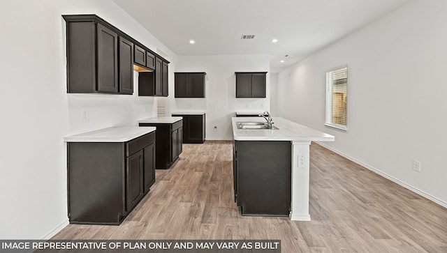 kitchen with a kitchen island with sink, sink, dark brown cabinets, and light hardwood / wood-style floors