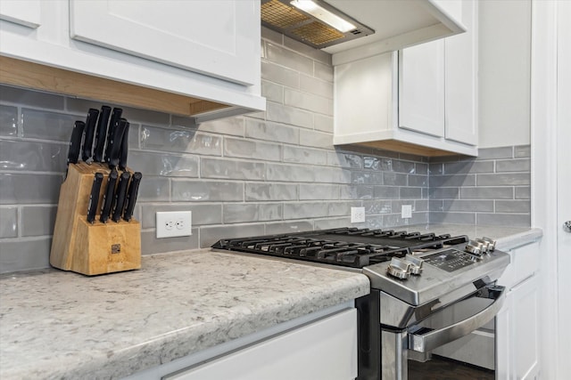 kitchen with wall chimney range hood, stainless steel gas range, backsplash, light stone counters, and white cabinets