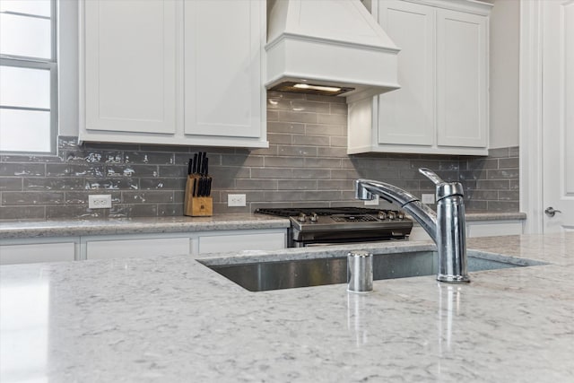 kitchen featuring decorative backsplash, light stone countertops, custom range hood, and white cabinets