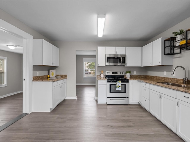 kitchen featuring sink, white cabinetry, dark stone countertops, stainless steel appliances, and light wood-type flooring