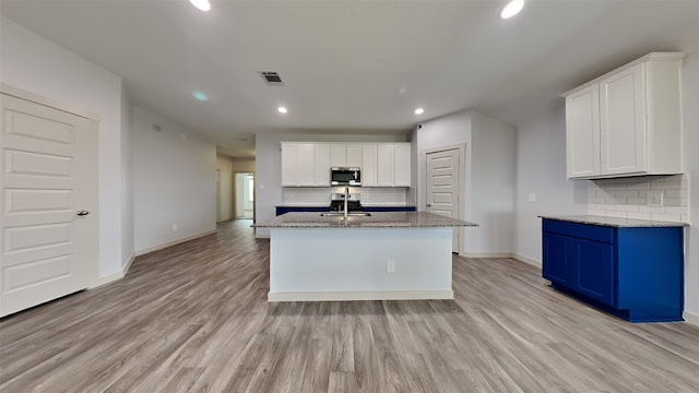 kitchen featuring a kitchen island with sink, sink, light stone countertops, and white cabinets