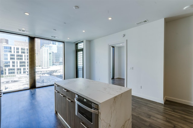 kitchen featuring oven, dark hardwood / wood-style flooring, expansive windows, a center island, and light stone countertops