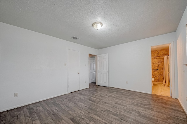 unfurnished bedroom with ensuite bathroom, a textured ceiling, and light wood-type flooring