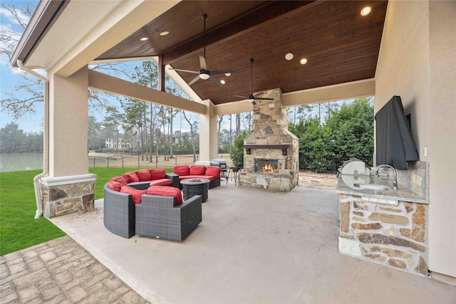 view of patio featuring exterior kitchen, an outdoor living space with a fireplace, ceiling fan, and a water view