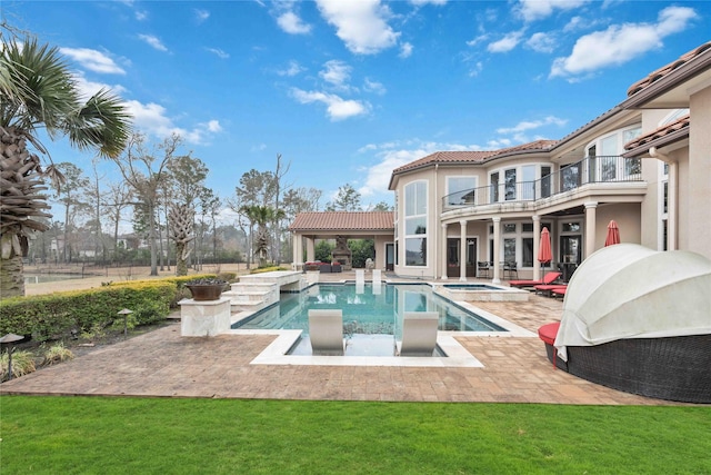 rear view of house featuring a balcony, a pool with hot tub, a patio, and a lawn