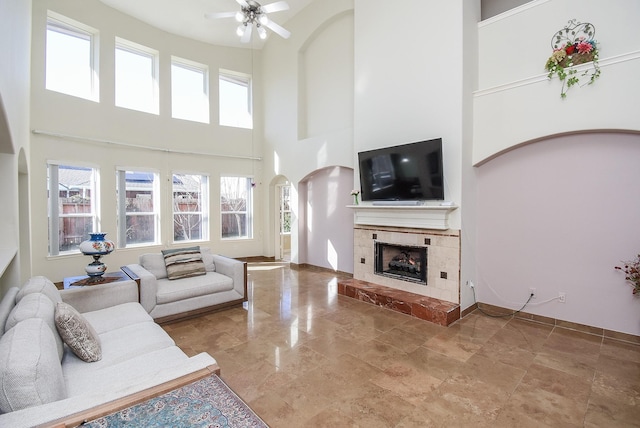 living room with a tile fireplace, a healthy amount of sunlight, ceiling fan, and a towering ceiling